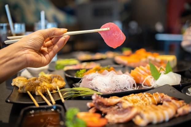 Hand holding tuna sashimi using chopsticks.