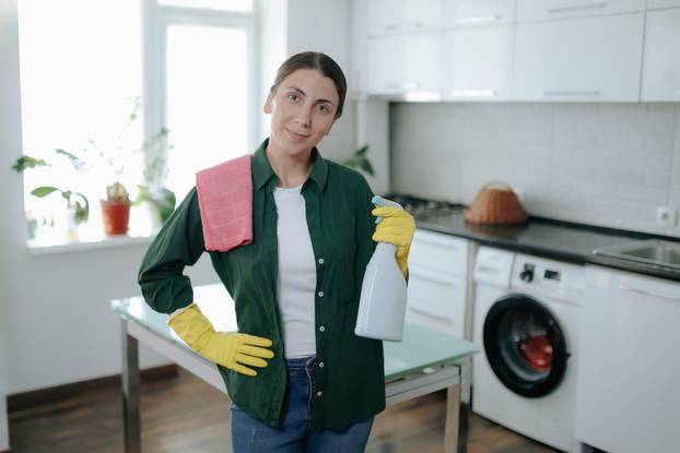 Joyful Young Woman in Yellow Gloves Smiling at Camera in Her Home Kitchen