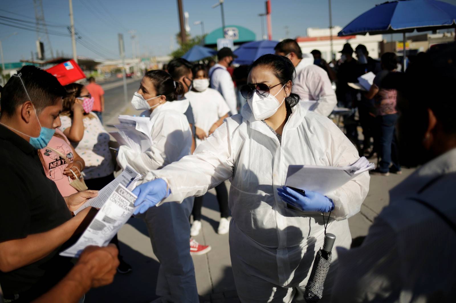 Personnel of an assembly factory, in protective gear, hands out job application forms to job seekers as the coronavirus disease (COVID-19) outbreak continues in Ciudad Juarez
