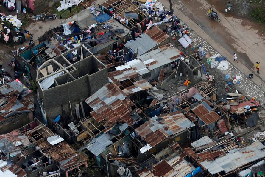 People walk down the street next to destroyed houses after Hurricane Matthew passes Jeremie, Haiti