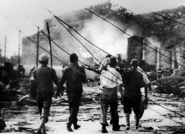 FILE PHOTO: Japanese air raid workers carry a victim of the atomic bomb away from smoking ruins in Hiroshima