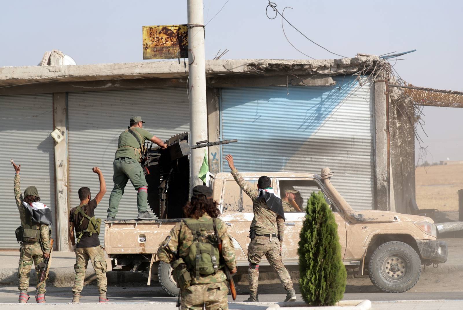 Turkey-backed Syrian fighters gesture as their comrade fires a weapon mounted on a truck in the town of Tal Abyad
