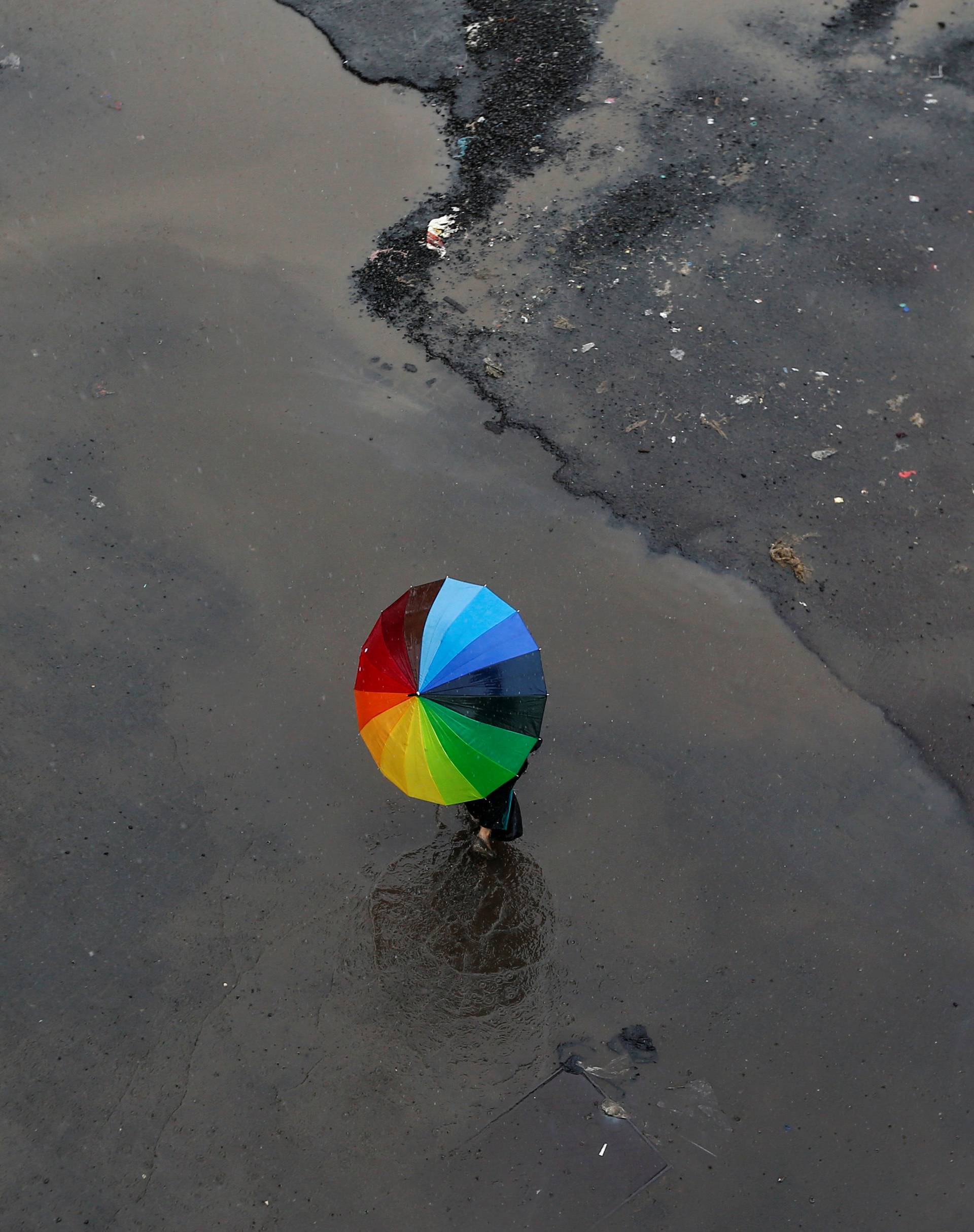 A woman carrying an umbrella crosses a flooded street as it rains in Mumbai