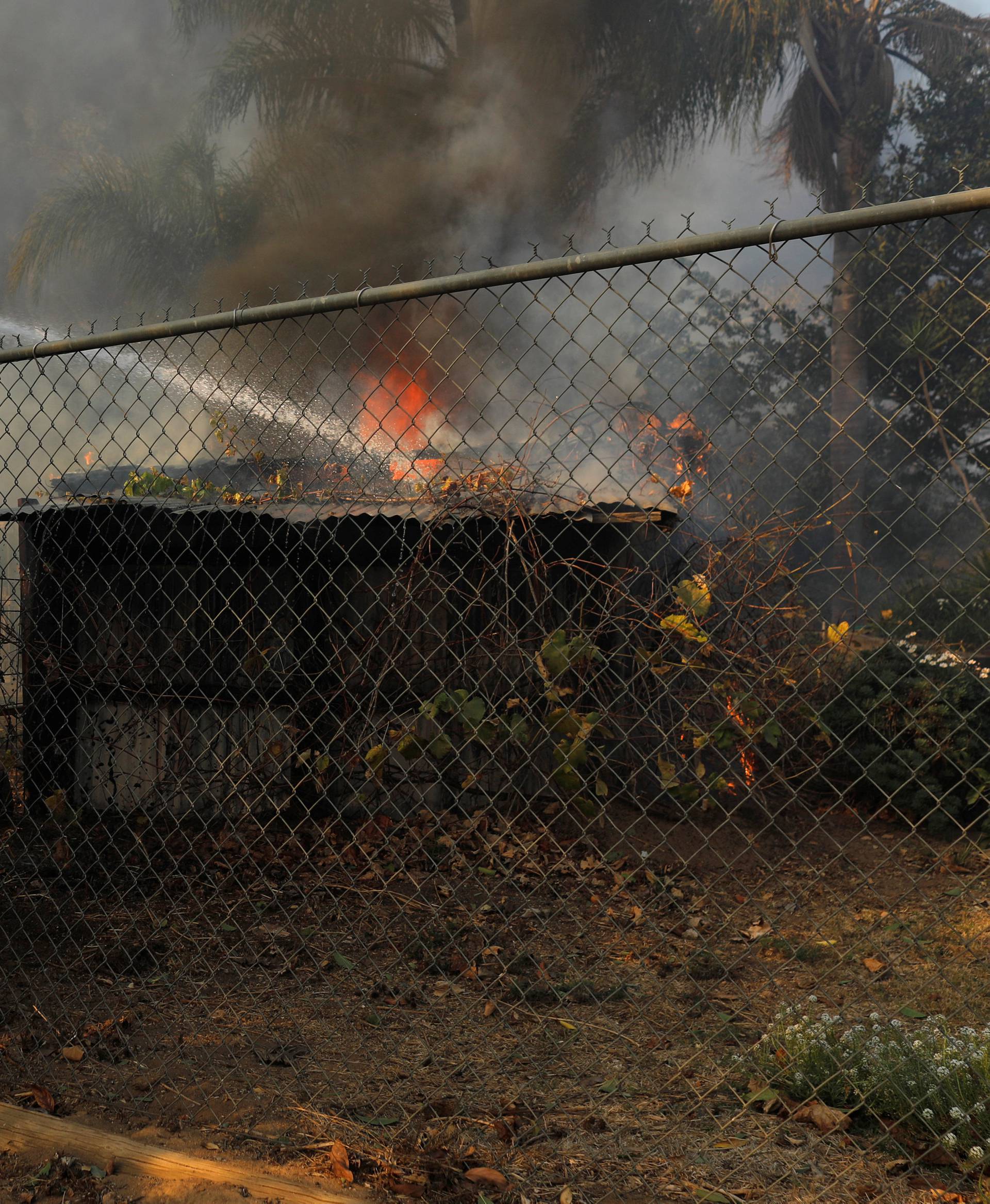 Firefighters jump a fence to try and save a burning home from the Lilac Fire, a fast moving wild fire, came through Bonsall, California