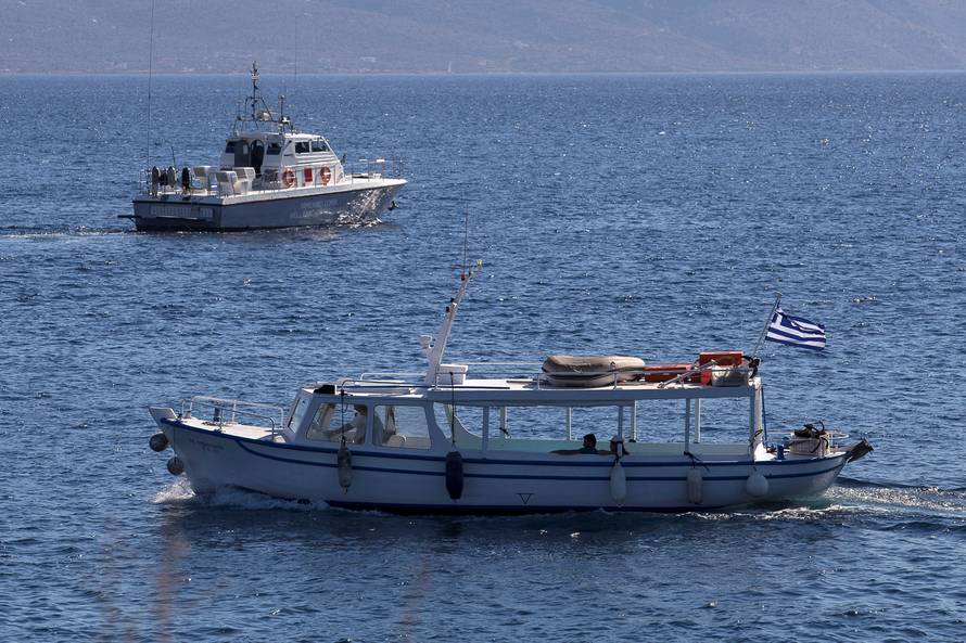 A coastguard boat inspect the area where four people, including a nine-year-old girl, died and at least five were injured after a boat with about 20 people on board collided with a speedboat off the Greek holiday island of Aegina close to Athens