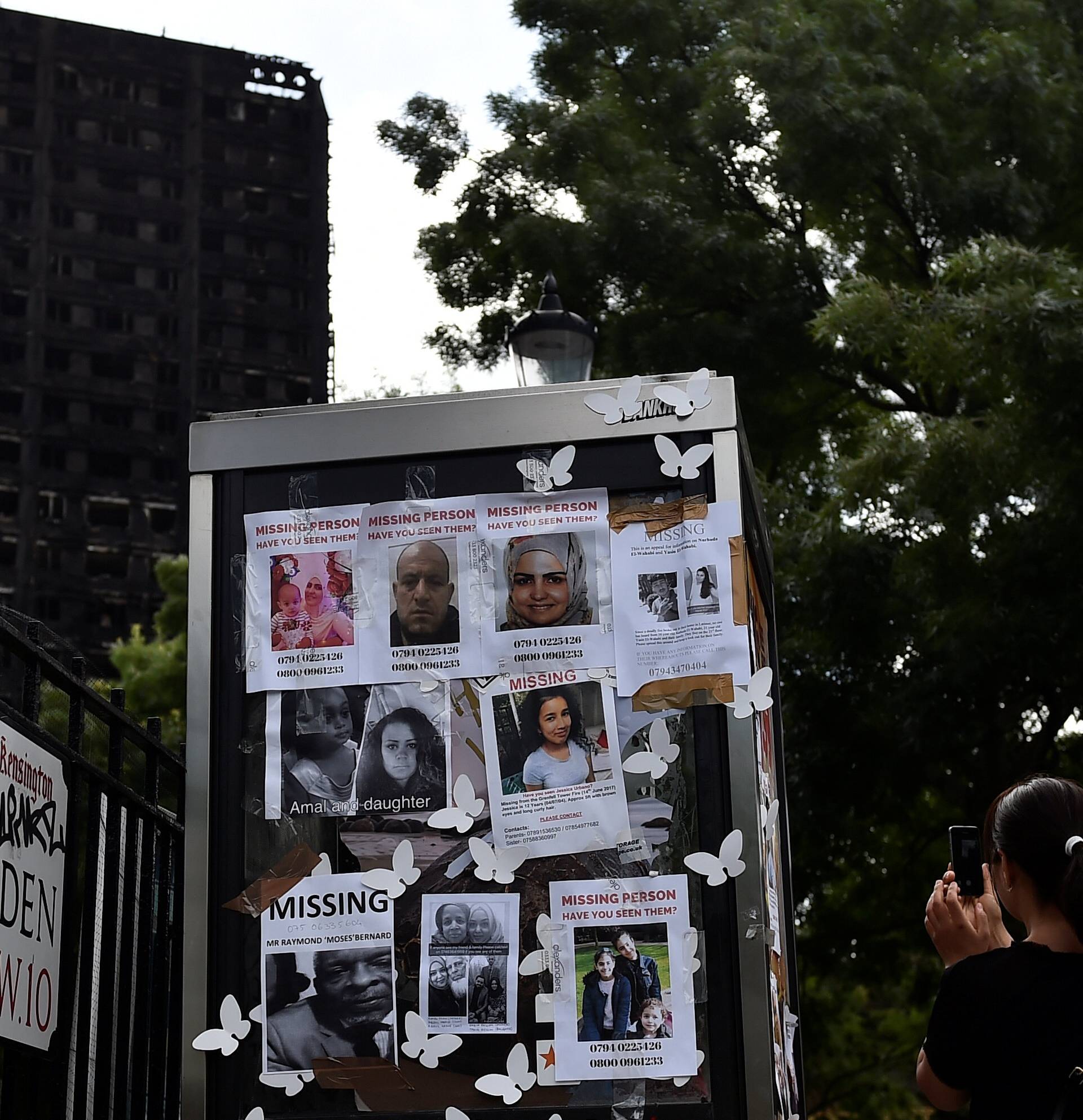 A woman photographs missing persons posters near the scene of the fire that destroyed the Grenfell Tower block, in north Kensington, West London