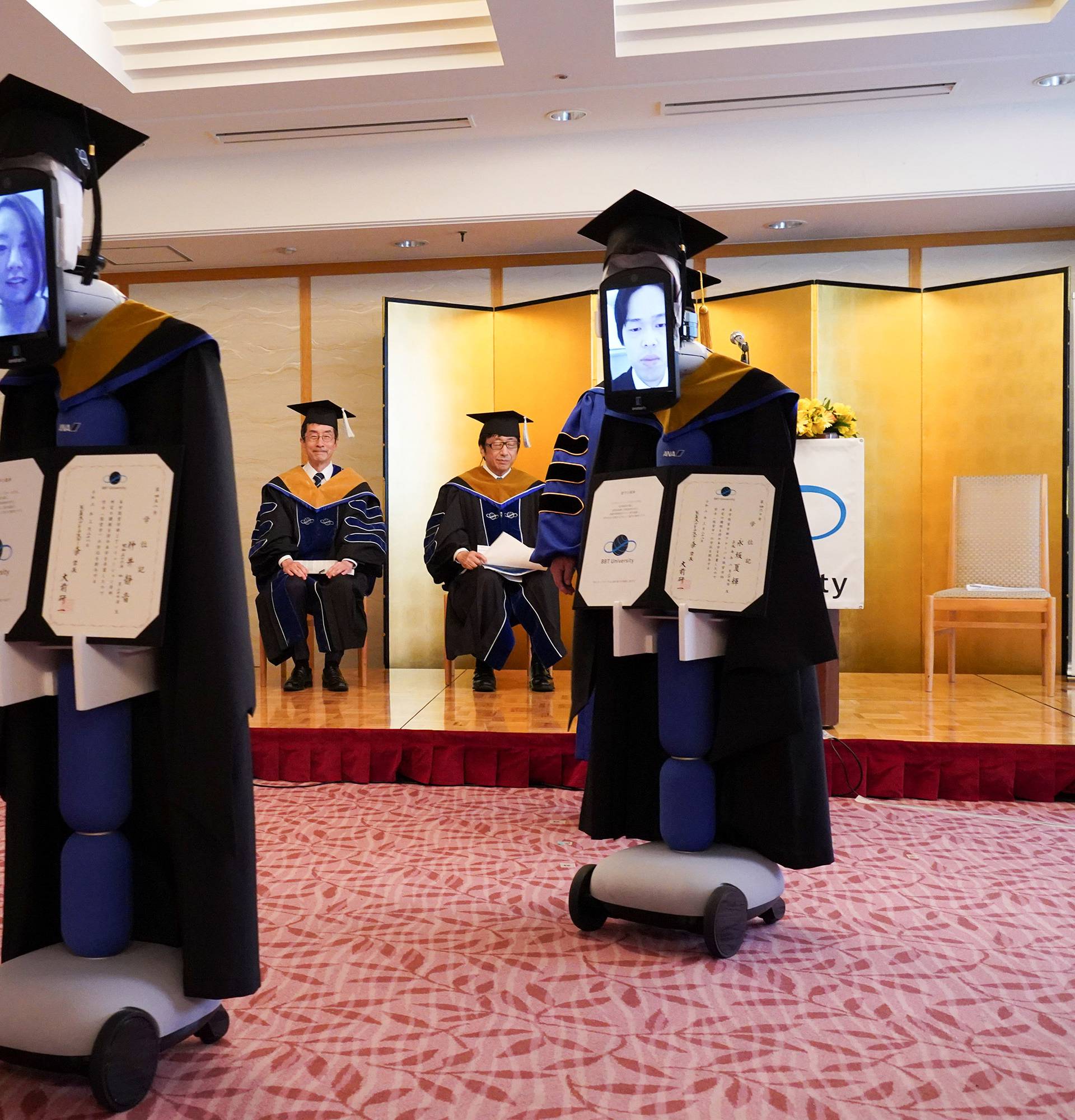 Ipads attached to 'newme' robots replacing graduating students' presence at a ceremony, wear graduation gowns and hats in Tokyo