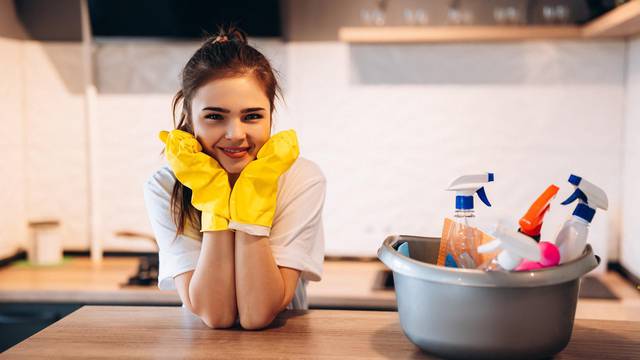 Pretty woman in protective yellow gloves is smiling in the kitchen while cleaning.