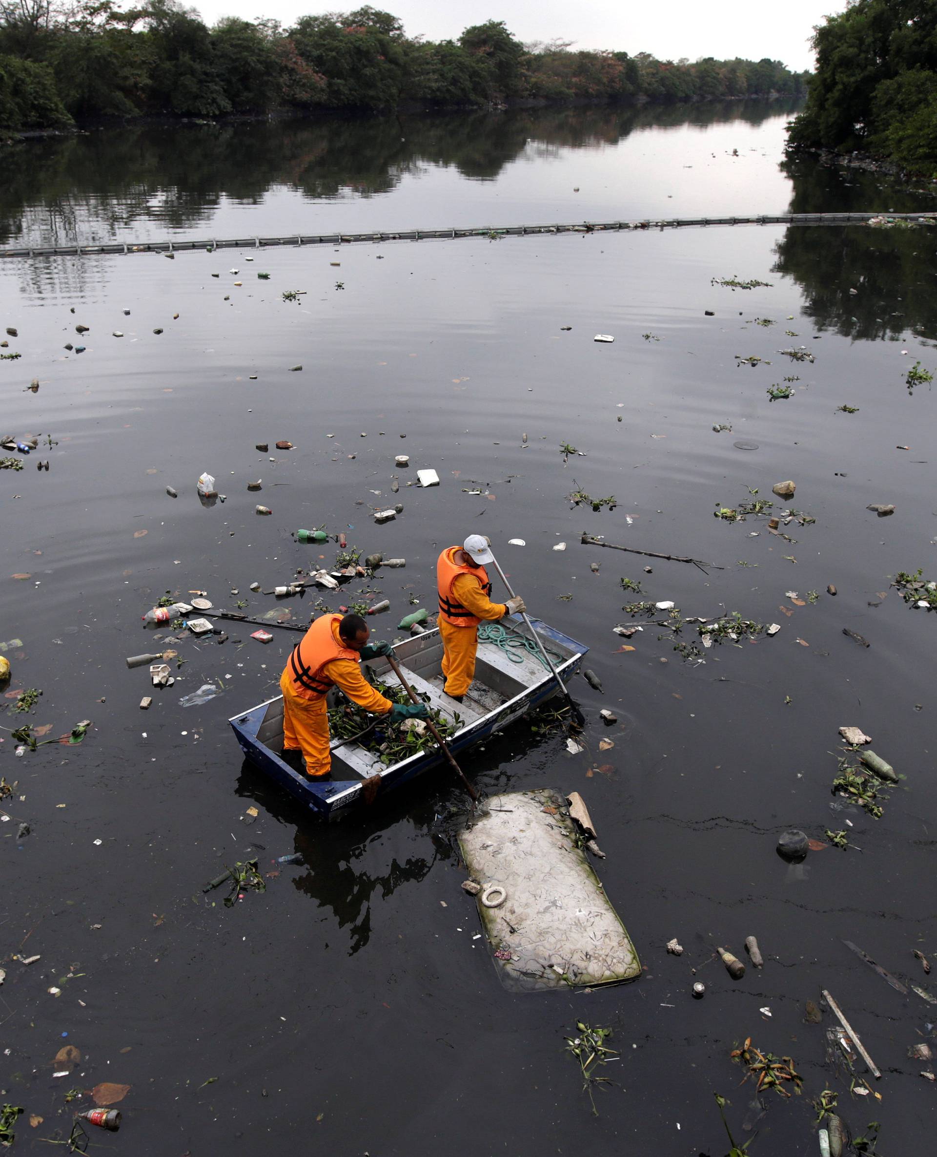 Men work cleaning up the garbage next to an ecobarrier at Meriti River which flows into Guanabara Bay, in Duque de Caxias, near Rio de Janeiro