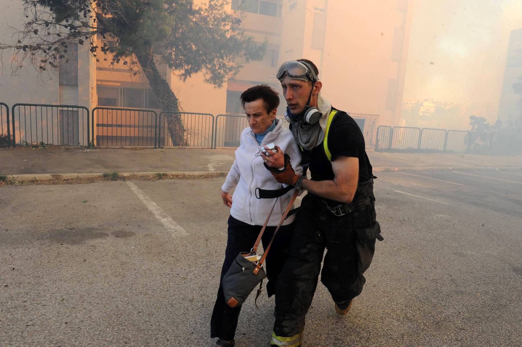 An emergency personnel member evacuates a woman as a wildfire burns in the northern Israeli city of Haifa, Israel 
