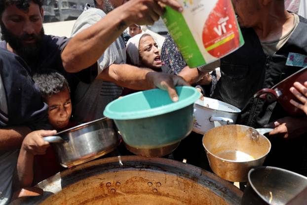 Palestinians wait to receive food cooked by a charity kitchen, in Gaza City