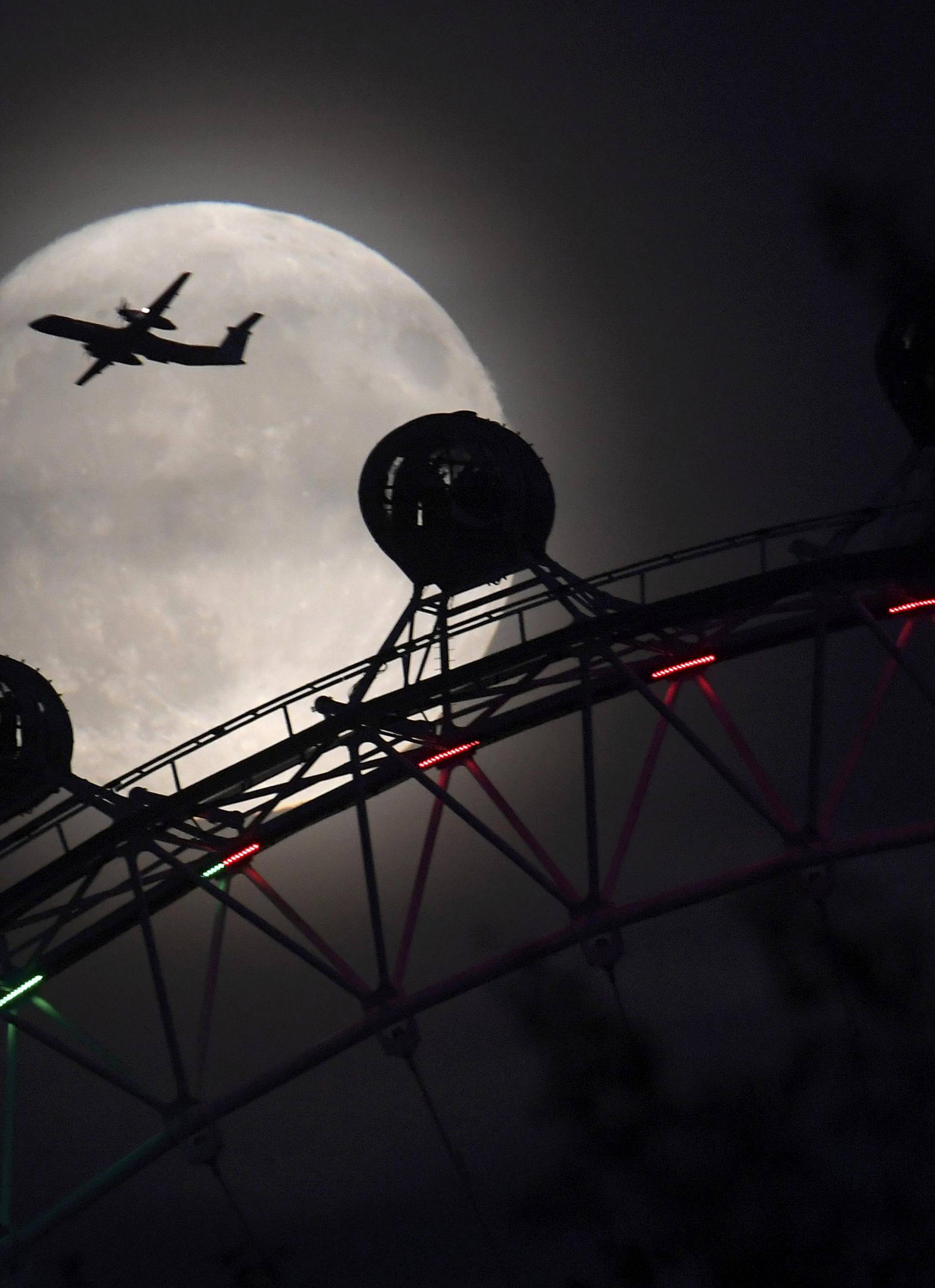 An aeroplane flies past the London Eye wheel, and moon, a day before the "supermoon" spectacle in London