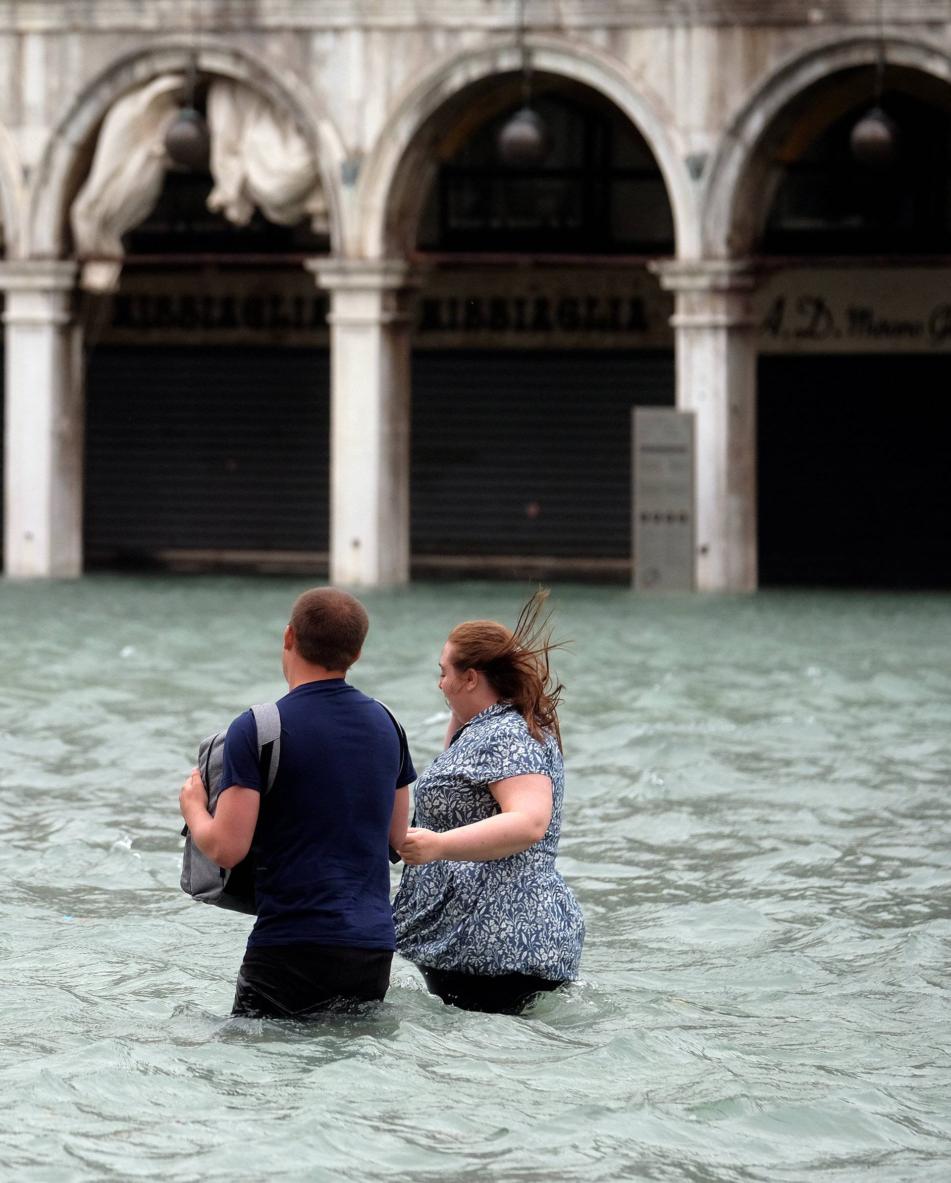 A couple walk in the flooded Saint Mark Square during a period of seasonal high water in Venice