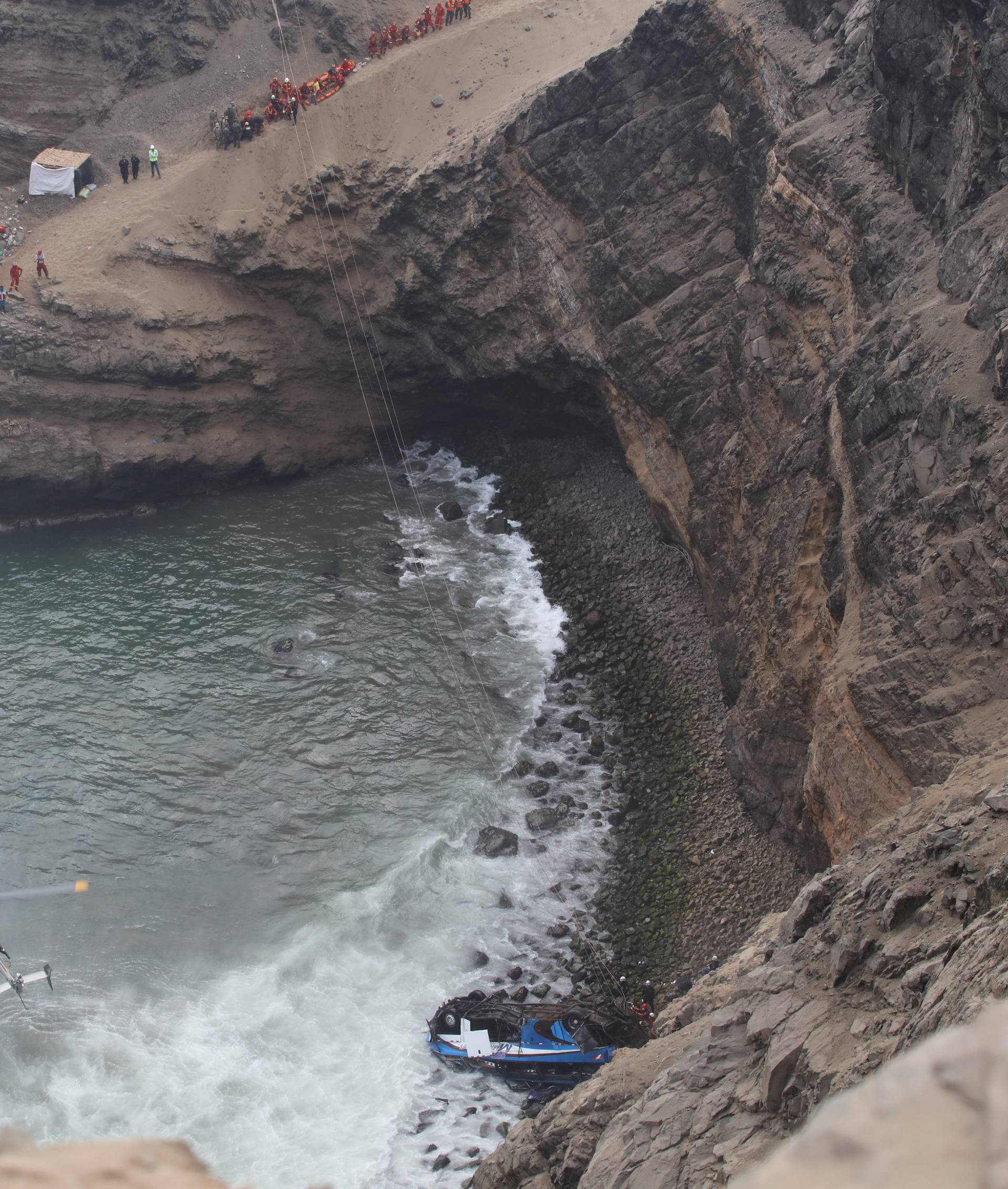 A helicopter helps rescue workers at the scene after a bus crashed with a truck and careened off a cliff along a sharply curving highway north of Lima