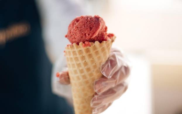 Waffle cone with delicious strawberry ice-cream in the hand. The seller puts a ball of ice-cream in a waffle cone by scoop or spoon