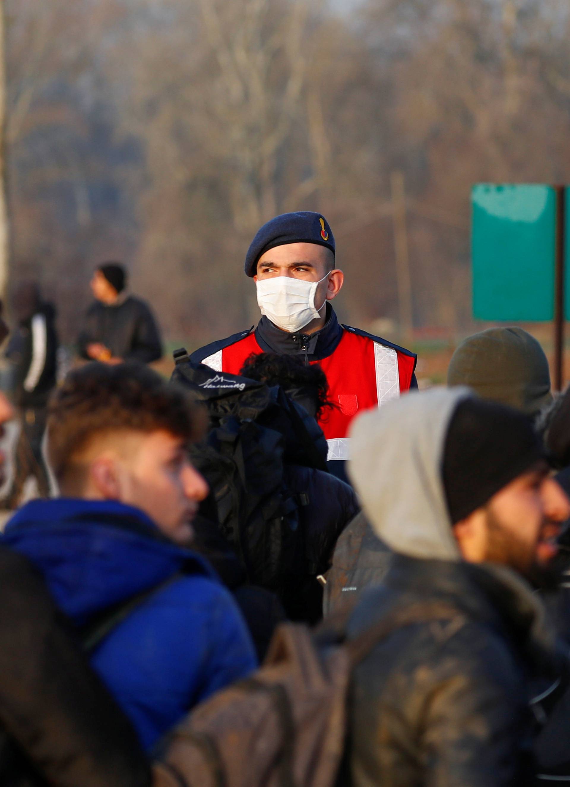 A Turkish gendarmerie officer wearing a face mask is seen as migrants walk next to the Turkey's Pazarkule border crossing with Greece's Kastanies, near Edirne
