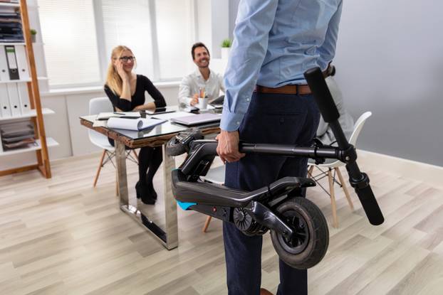 Person Carrying Electric Scooter In Folded Position At Office