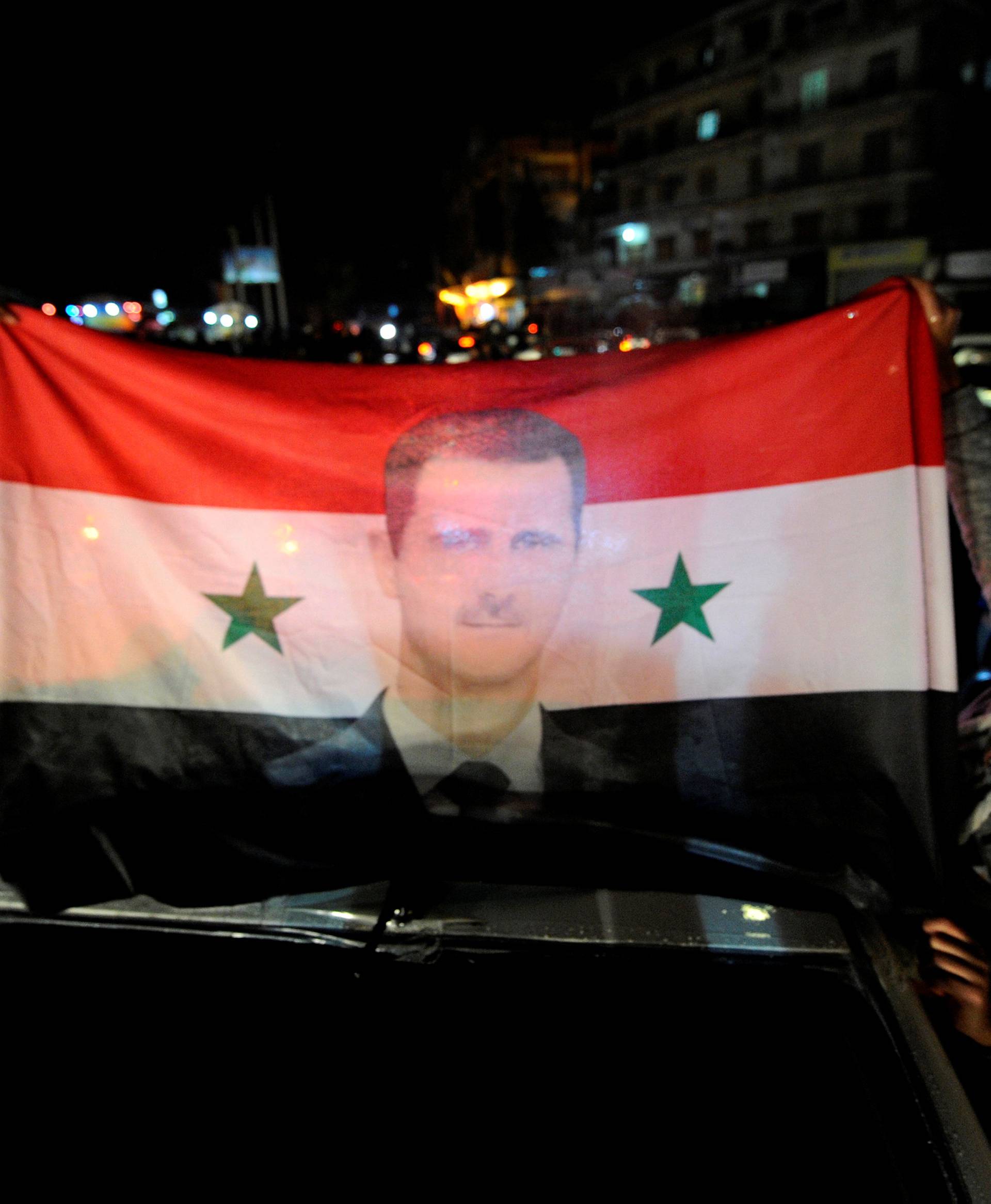 Supporters of Syria's President Bashar al-Assad carry a Syrian national flag with his picture as they tour the streets in celebration of what they say is the Syrian army's victory against the rebels in Aleppo
