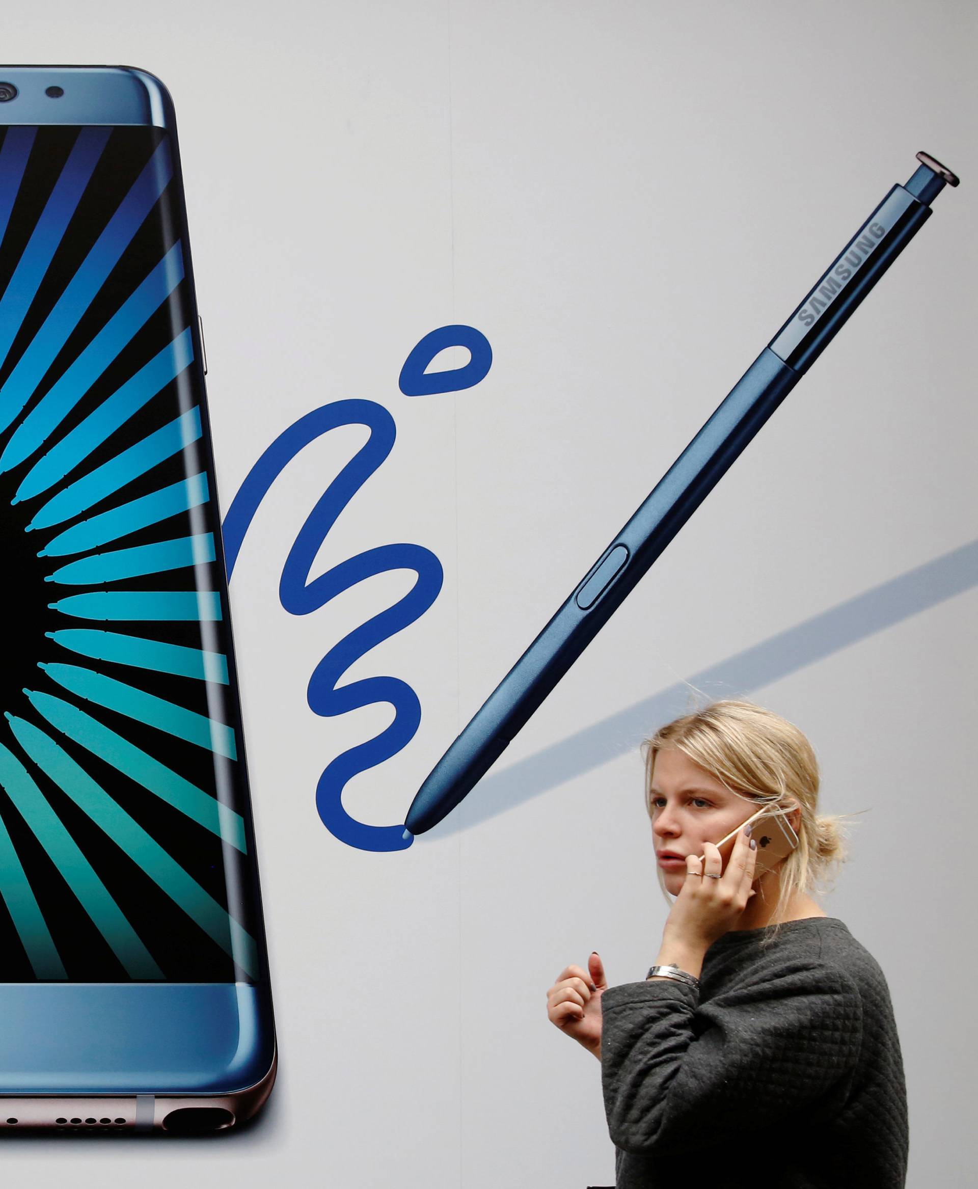 A woman speaks on an phone as she passes an advert for the Samsung Galaxy Note 7 in London