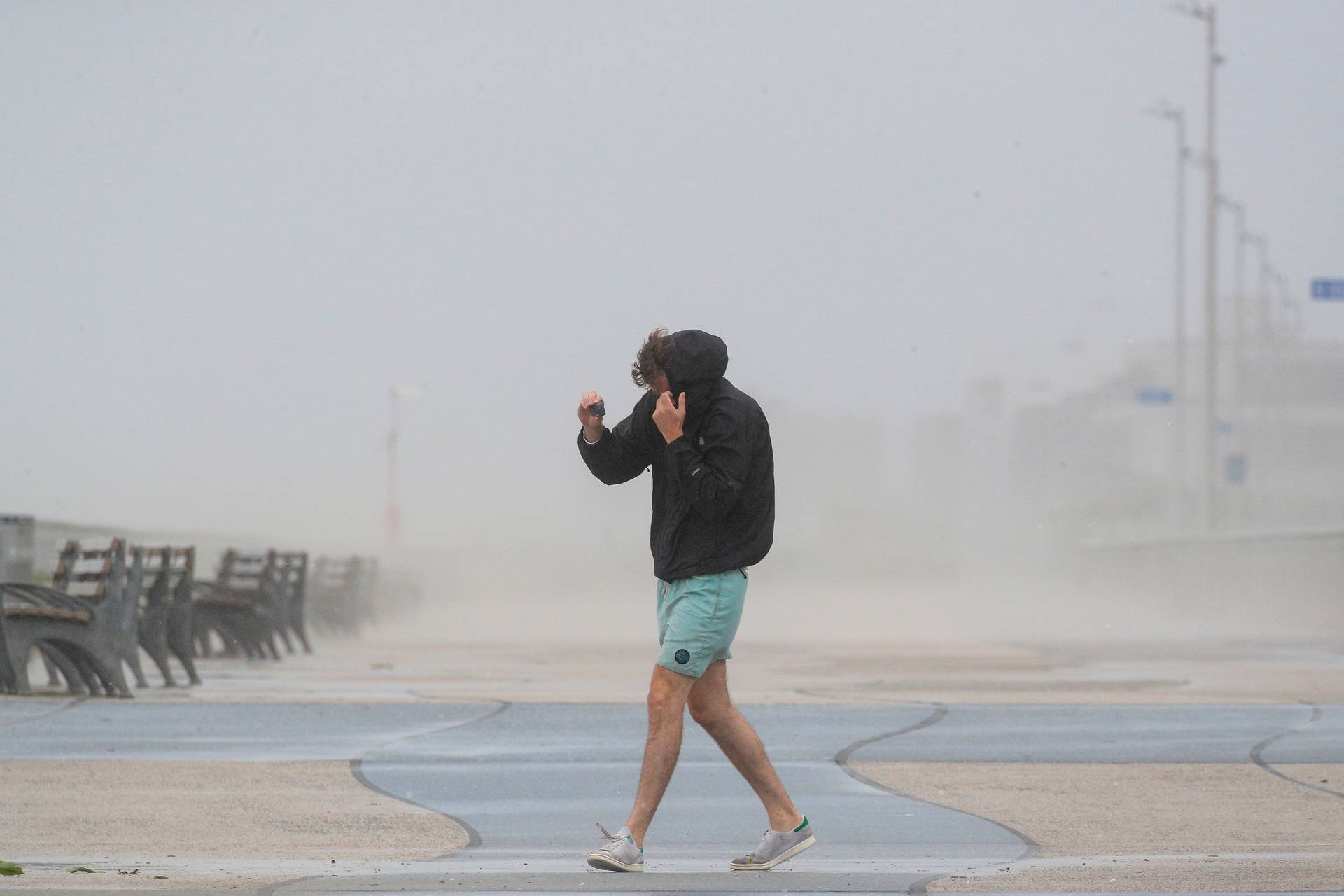 A man shields himself from the winds from Tropical Storm Isaias while walking on the boardwalk in the Rockaway area of Queens in New York