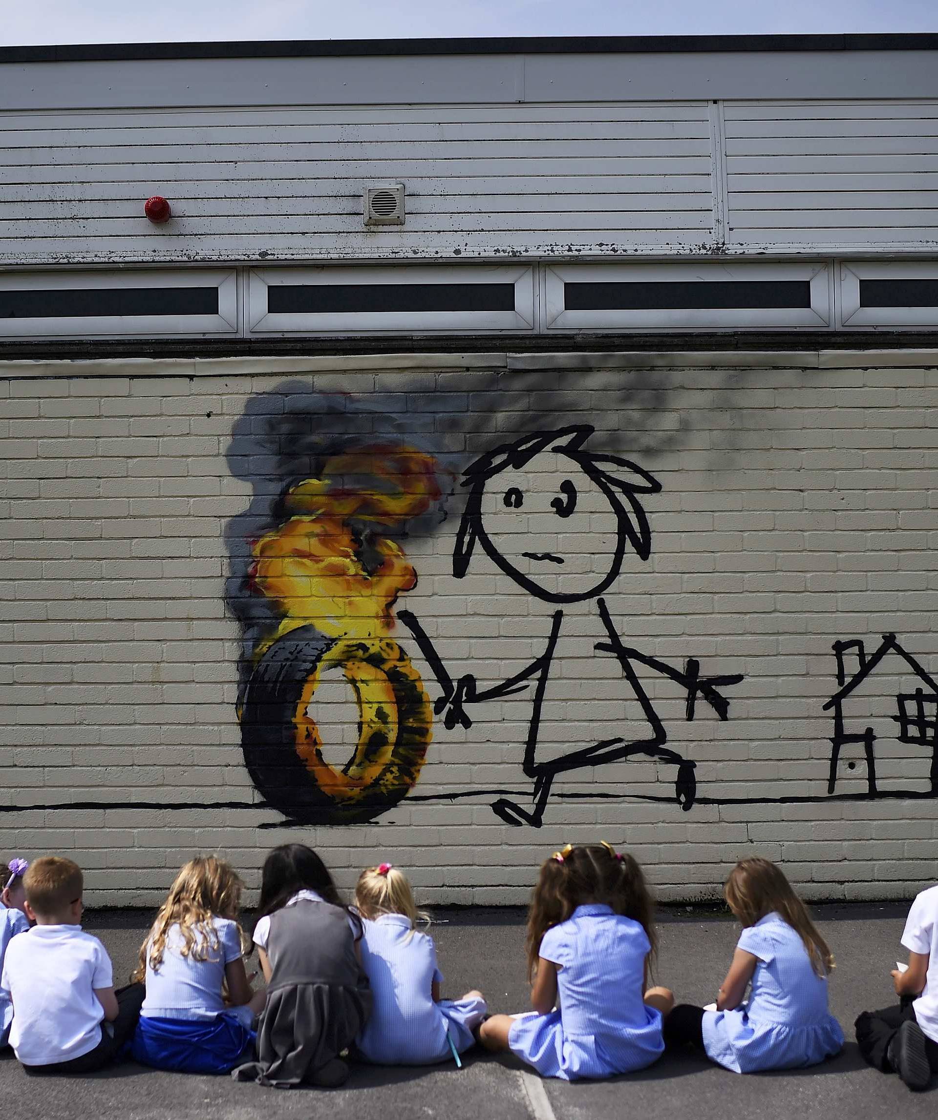 Reception class school children sit in a row as they draw a mural attributed to Banksy in Bristol