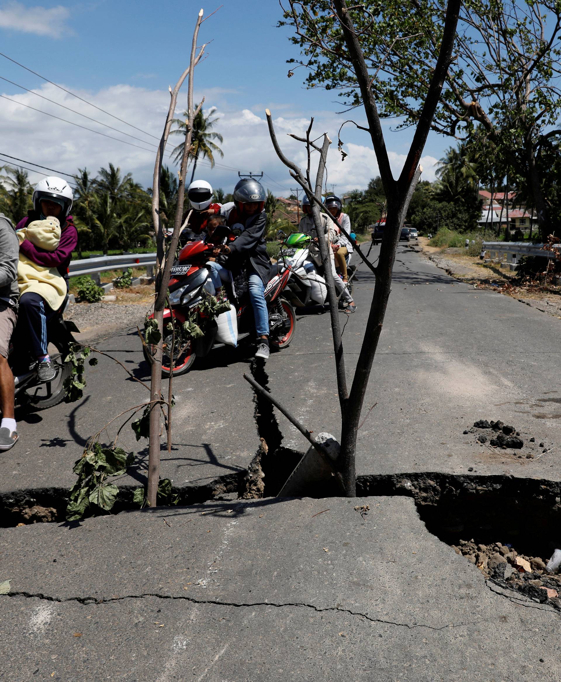 A family rides on a motorcycle through a crack on the street at Kayangan district after earthquake hit on Sunday in North Lombok
