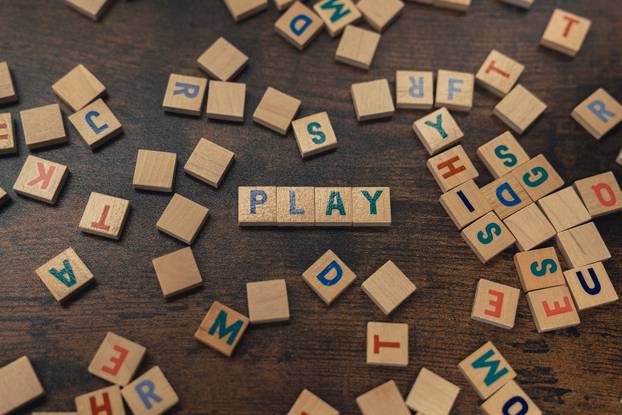 Scattered wooden word play. Colorful square letters on a dark wooden table creating the word PLAY. Leisure activity concept.