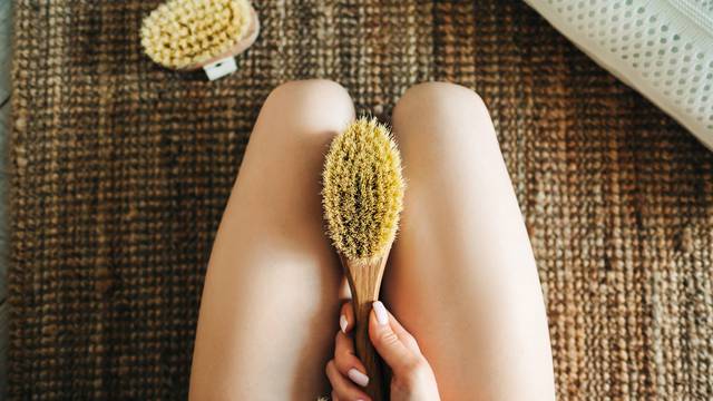 Woman holding wooden brush and doing dry massage on her feet. Self care conceptWoman holding wooden brush and doing dry massage on her feet. Self care concept