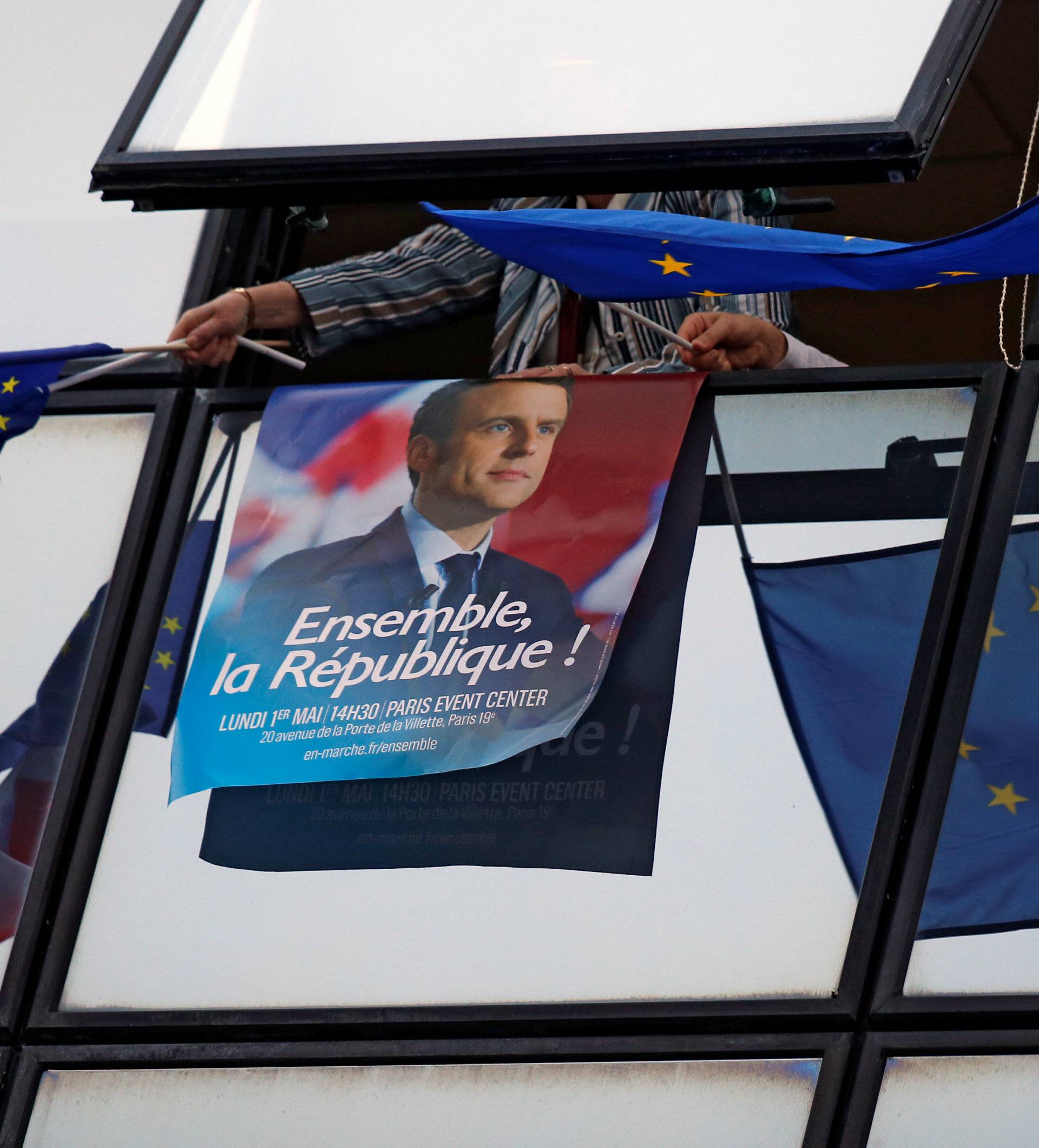 A supporter holds a campaign poster of Emmanuel Macron and European Union flags after results were announced in the second round of 2017 French presidential election at the campaign headquarters in Paris