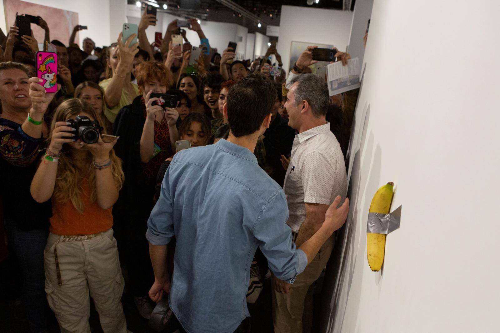 Art Basel visitors use their phones in front of a banana attached with duct-tape that replaces the artwork 'Comedian' by the artist Maurizio Cattelan, which was eaten by David Datuna, in Miami Beach