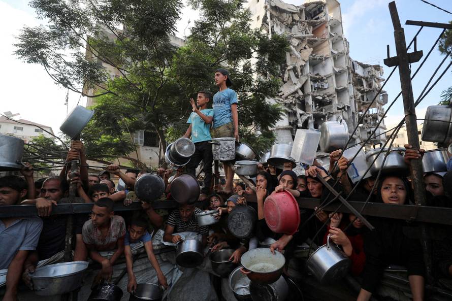 FILE PHOTO: Palestinians wait to receive food from a charity kitchen, amid a hunger crisis, in Gaza City