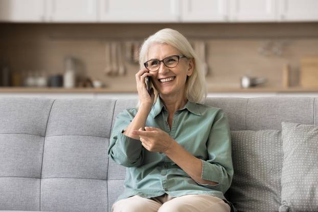 Older,Woman,Sits,On,Sofa,In,Living,Room,Talking,On