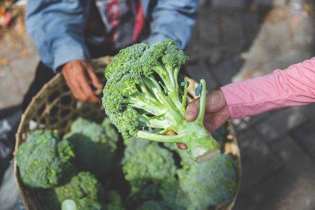 hand picking a broccoli in a market