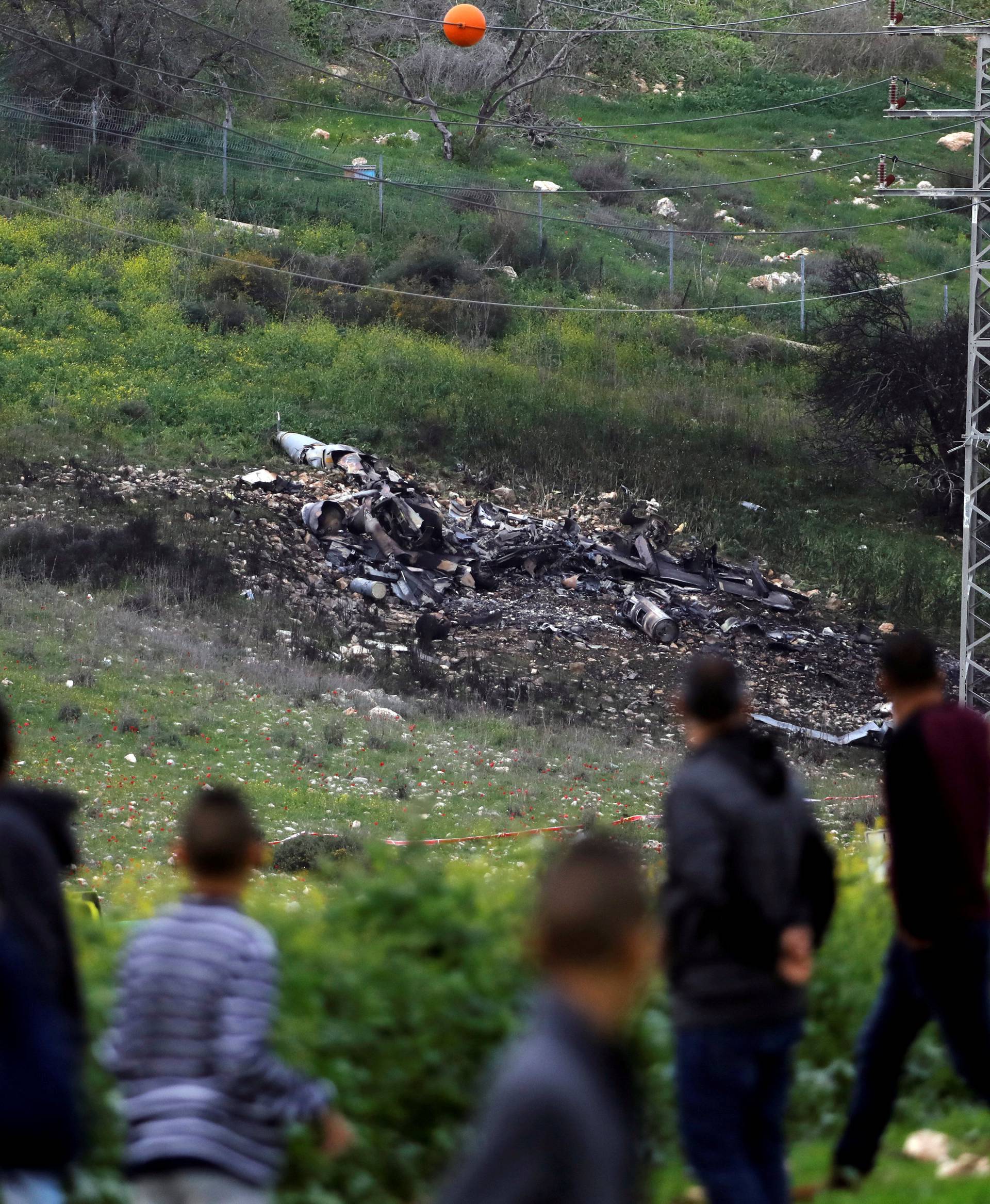 Bystanders look at the remains of an F-16 Israeli war plane near the village of Harduf