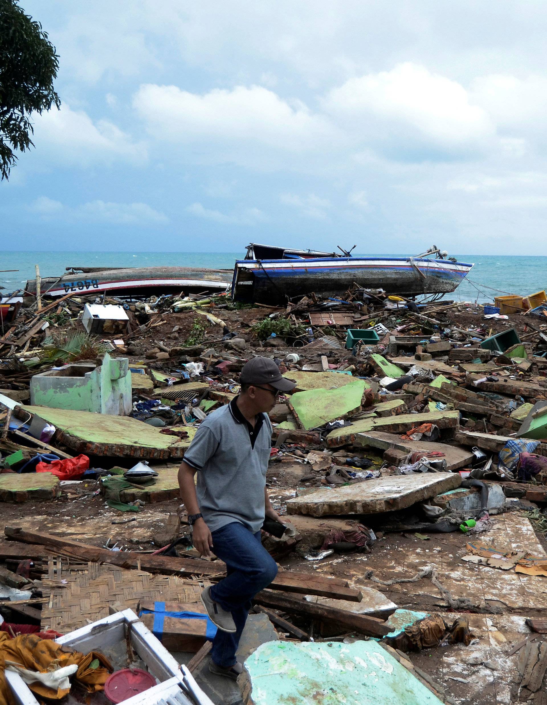 A local walks as he searches for his items among debris after a tsunami hit at Rajabasa district in South Lampung