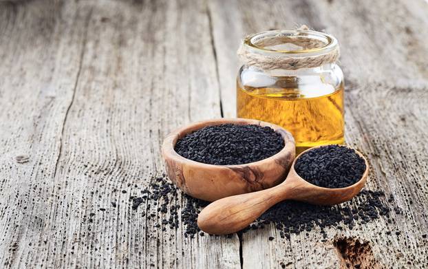 Black cumin oil with seeds on wooden background