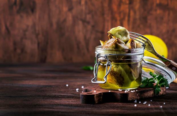 Canned artichokes in olive oil, in glass jar, rustic wooden kitc
