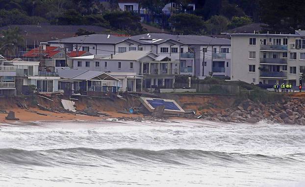 Officials stand near a swimming pool and houses that suffered damage after severe weather that brought strong winds and heavy rain to the east coast of Australia at Collaroy beach in Sydney, Australia