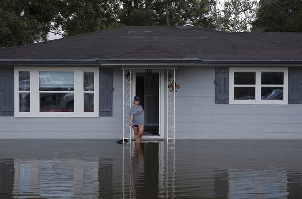 A woman smokes a cigarette on the front porch of a home surrounded by floodwaters in Sorrento, Louisiana