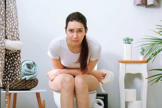 Young,Woman,Suffering,From,Constipation,On,Toilet,Bowl,At,Home
