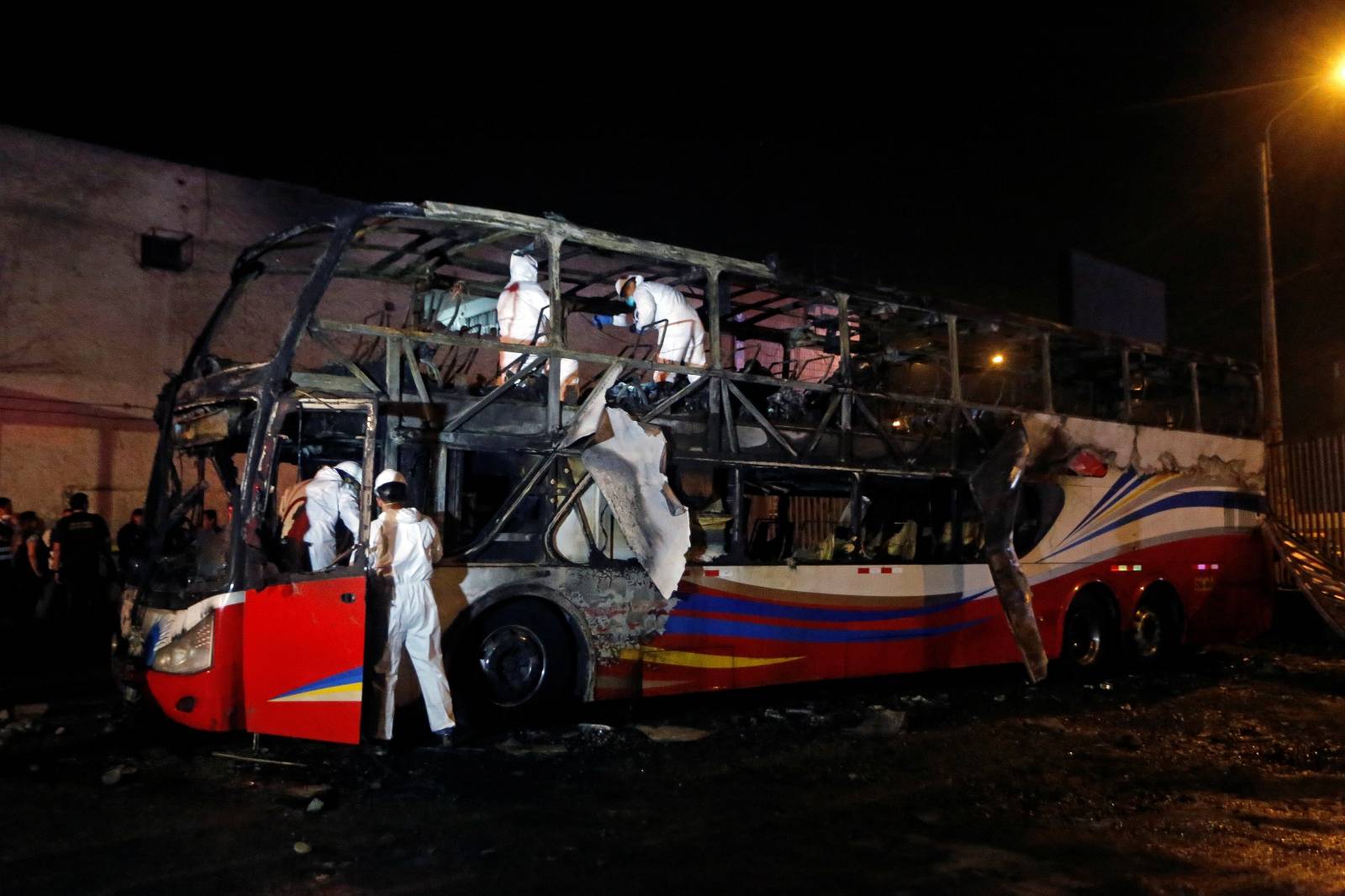 Peruvian investigators work next to a burnt bus on a street in Lima