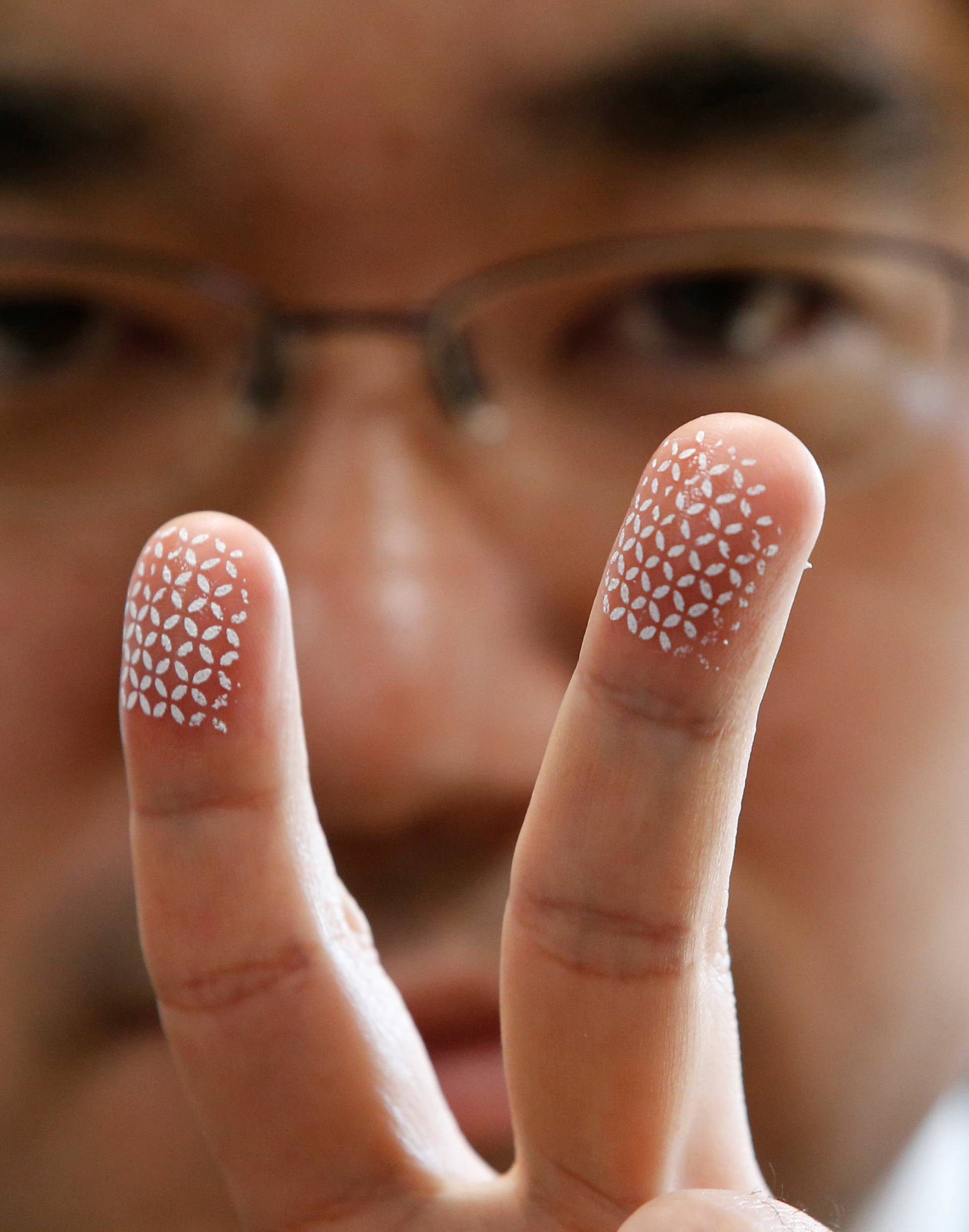 Echizen, a professor at Japan's National Institute of Informatics, poses to a photographer as he gestures with his fingers covered with a home-made biometric jammer during a demonstration of his experiment for Reuters in Tokyo