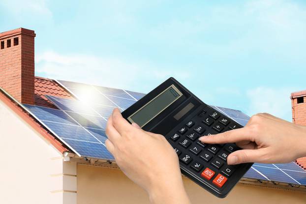 Woman,Using,Calculator,Against,House,With,Installed,Solar,Panels.,Renewable