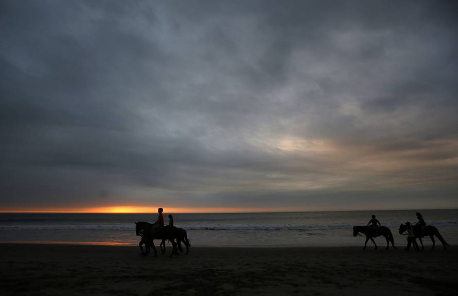 People riding horses by shoreline of the tourist beach of Mancora in Piura