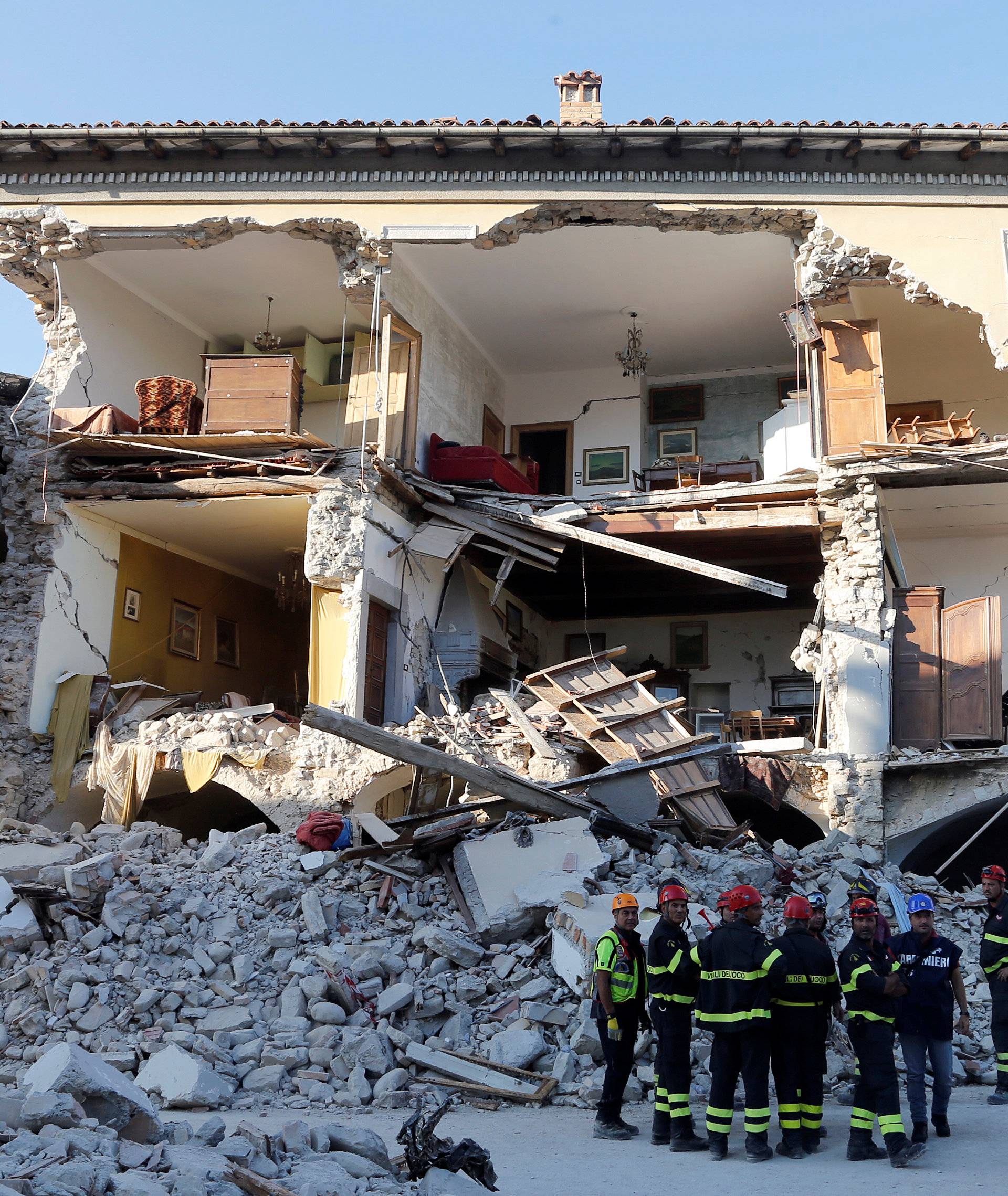 Firefighters stand next a collapsed house following an earthquake in Amatrice