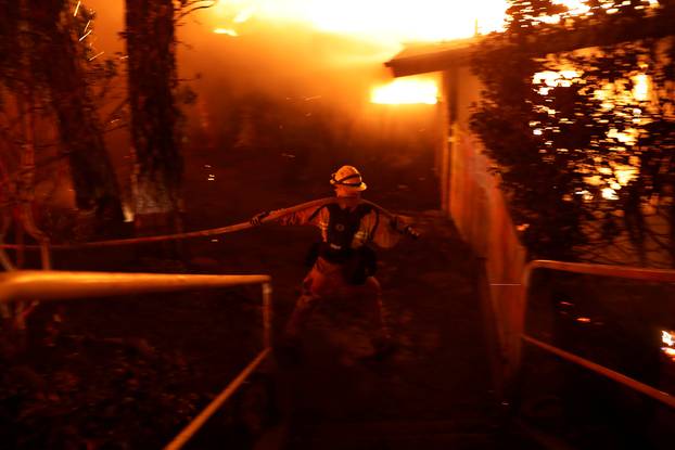 A firefighter drags a hose as he battles the Camp Fire in Paradise