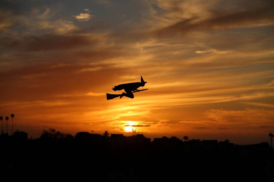 A remote-controlled plane in the form of a witch flies over a neighborhood as the sun sets during Halloween in Encinitas
