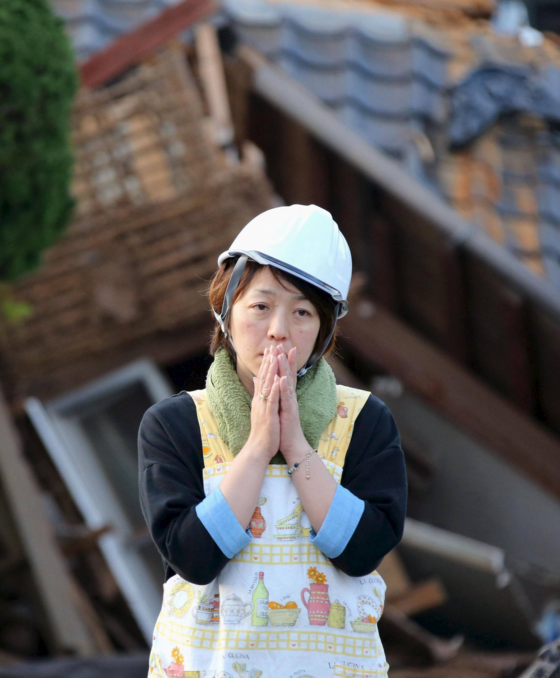 Woman reacts in front of collapsed house caused by an earthquake in Mashiki town