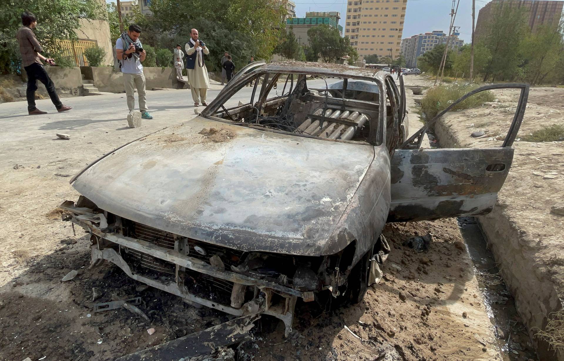 Afghan men take pictures of a vehicle from which rockets were fired, in Kabul