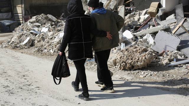 Syrian father Nader Fadil walks with his sister near the rubble of damaged buildings in Jableh